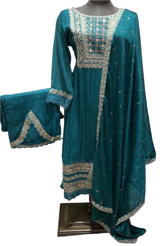 The outfit consists of three pieces: a long tunic top adorned with detailed embellishments around the neckline, sleeves, and hemline; a pair of matching trousers and a sheer dupatta